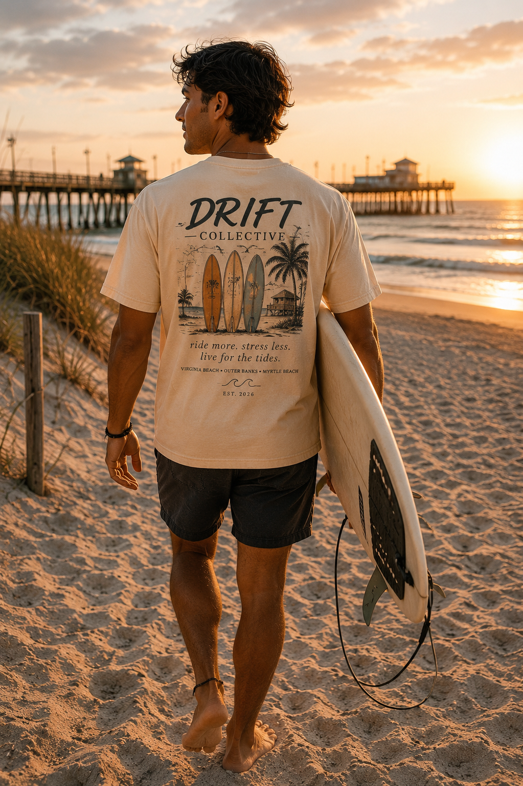 Model carrying a surfboard on the beach wearing the back graphic of the cream Drift Collective tee